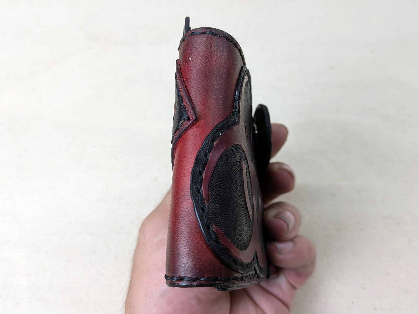 Handmade post-apocalyptic leather wallet held in hand, showing top view to highlight thickness.