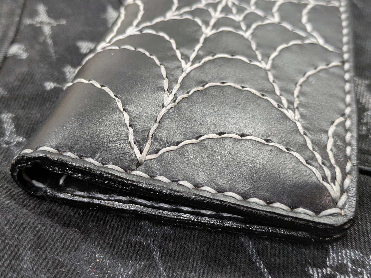 Close-up of the black leather long wallet's folded edge, showcasing the sturdy stitching and continuation of the spiderweb embroidery.