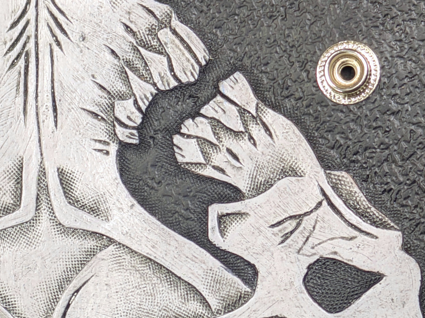 Close-up detail of the white skull design on the black leather wallet, showcasing the intricate engraving and texture, with a view of the snap button closure.