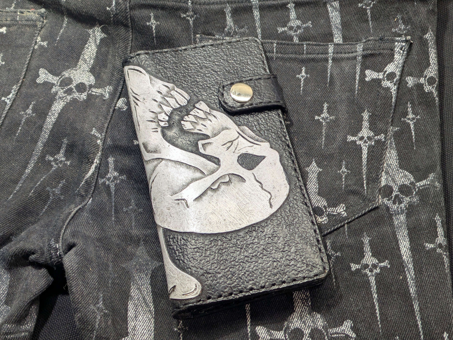 Front view of black leather wallet with silver double skulls Ace of Spades design, textured leather background, and snap button closure.