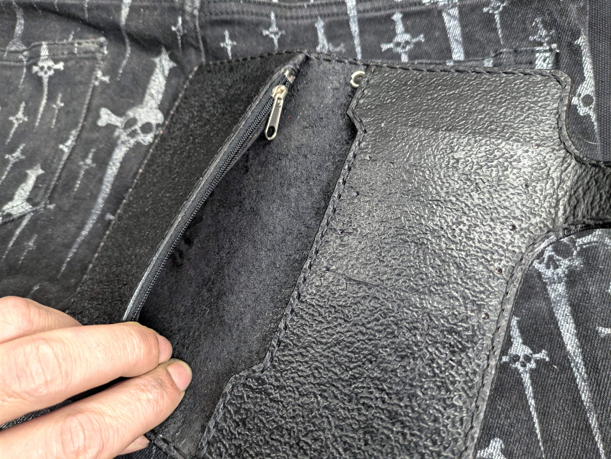 Hand holding open black leather wallet, interior view displaying note compartments and zippered coin pocket. Angled perspective shows textured leather and wallet features.