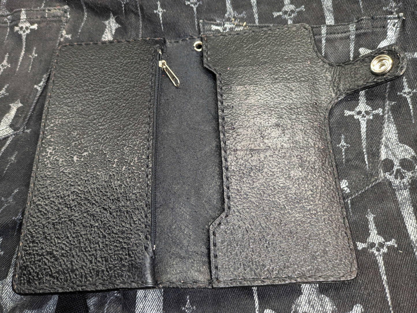 Interior view of the open black leather wallet, featuring card slots, bill compartments, and a zippered coin pocket. The wallet interior has a consistent textured black background.