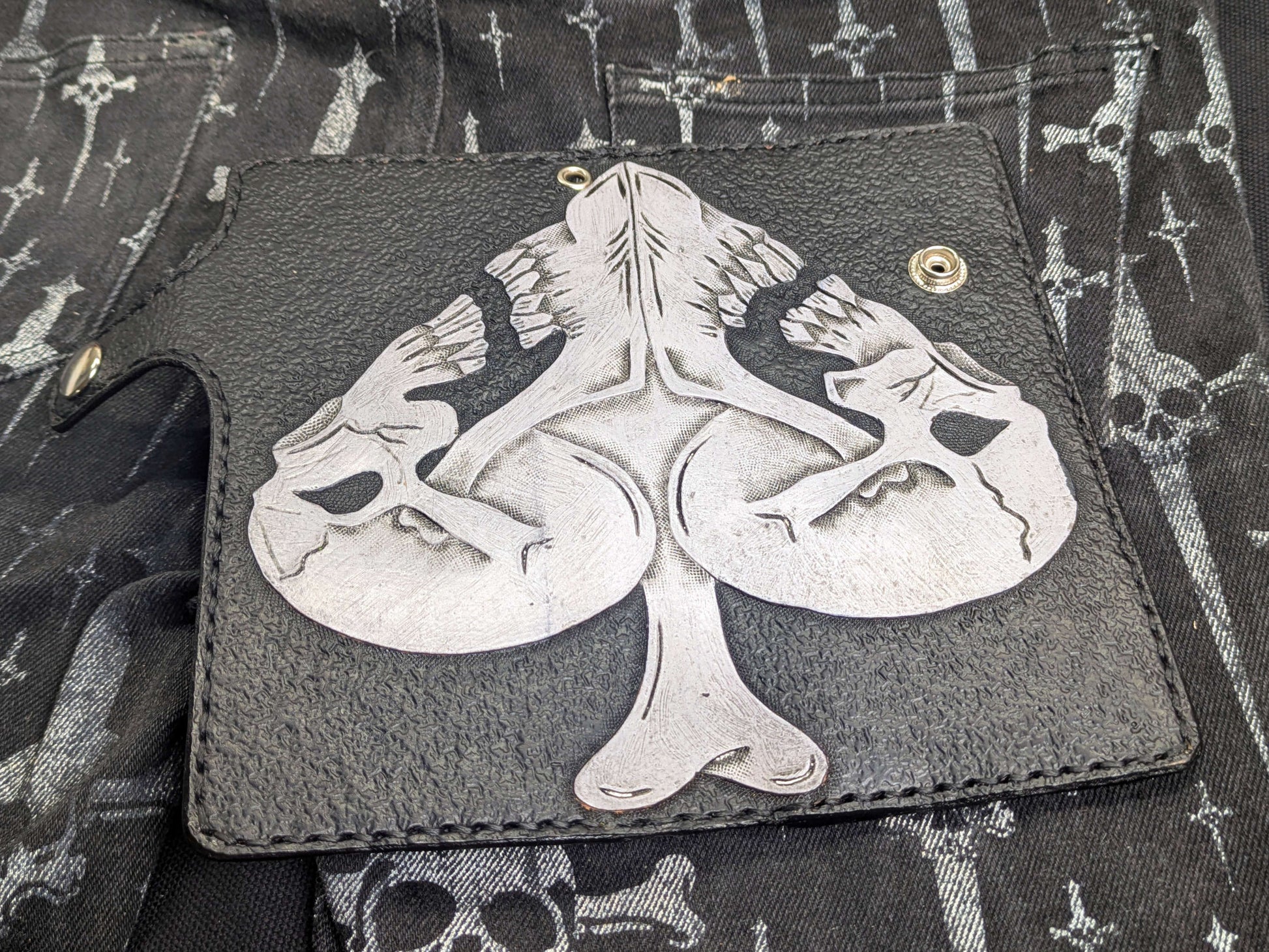 Fully open black leather wallet, angled view showcasing the complete Ace of Spades design with two white skulls and center bone. Textured leather interior and visible stitching details.