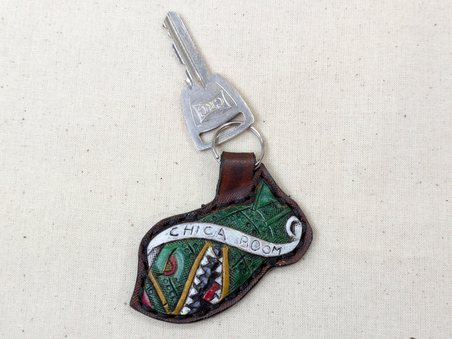 Keychain with decorative design and 'Chica Boom' text on a textured beige background