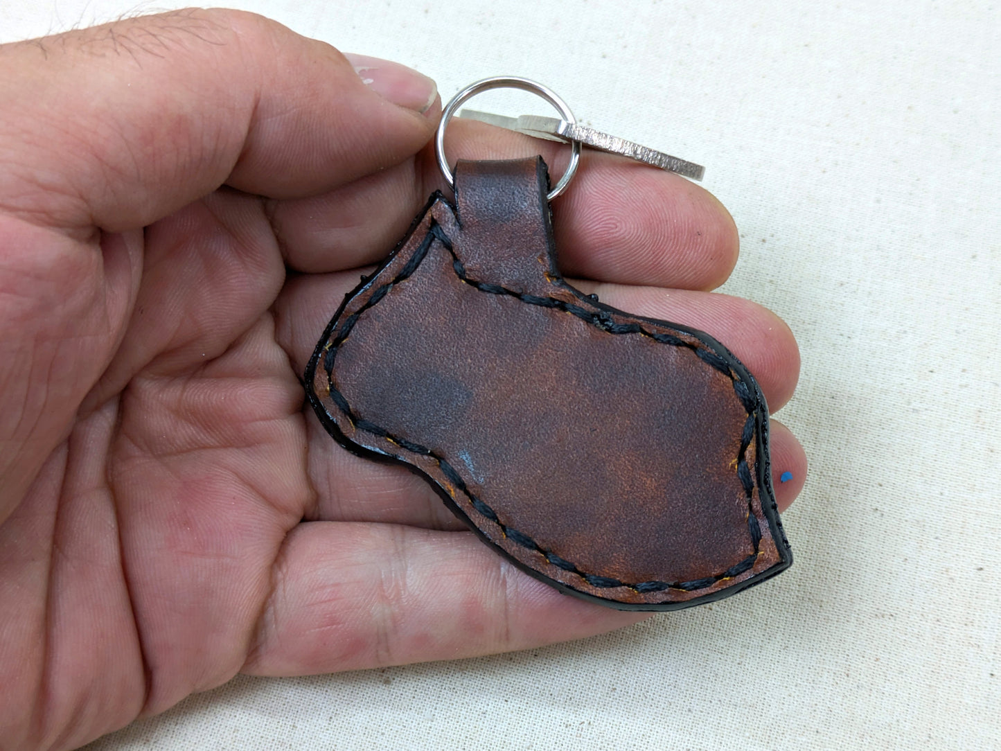 Brown leather keychain held in a hand against a light background