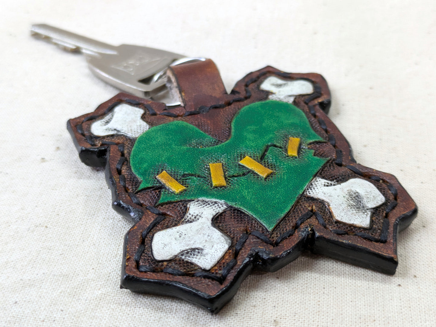 Handmade leather keychain with a detailed engraved skull design, in brown tones, with a metal keyring, on a light fabric background.