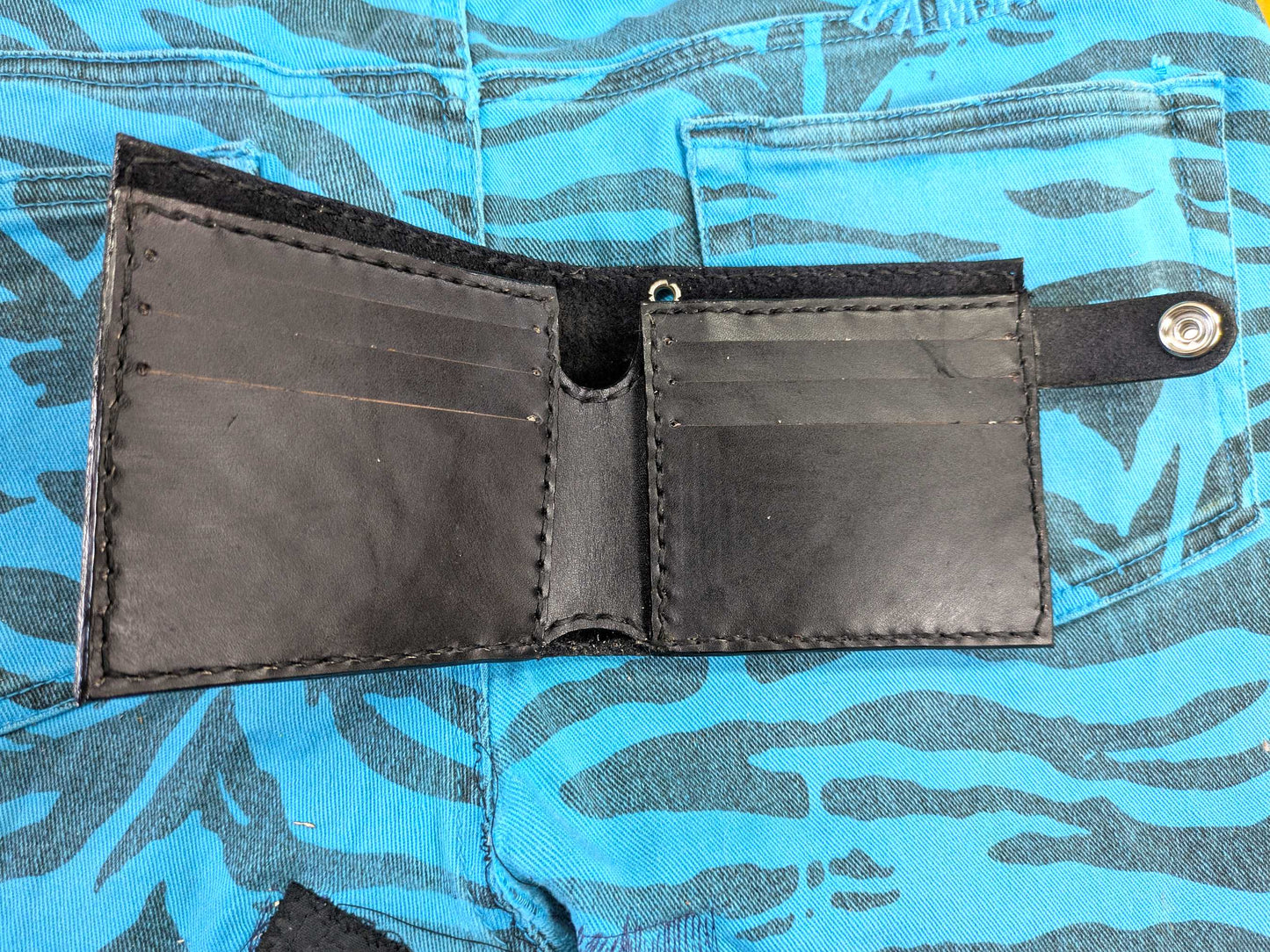 Open black leather bifold wallet, showing the interior with six card slots and a note compartment, with black hand-stitching, on a blue zebra-patterned fabric.
